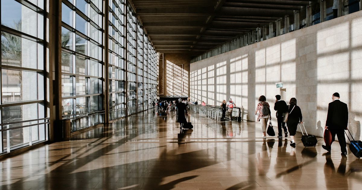 Putnici sa prtljagom prolaze kroz osvetljen aerodromski terminal